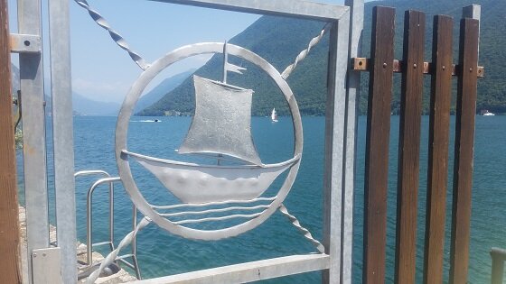 A decorative boat on a gate and Lugano lake in the background