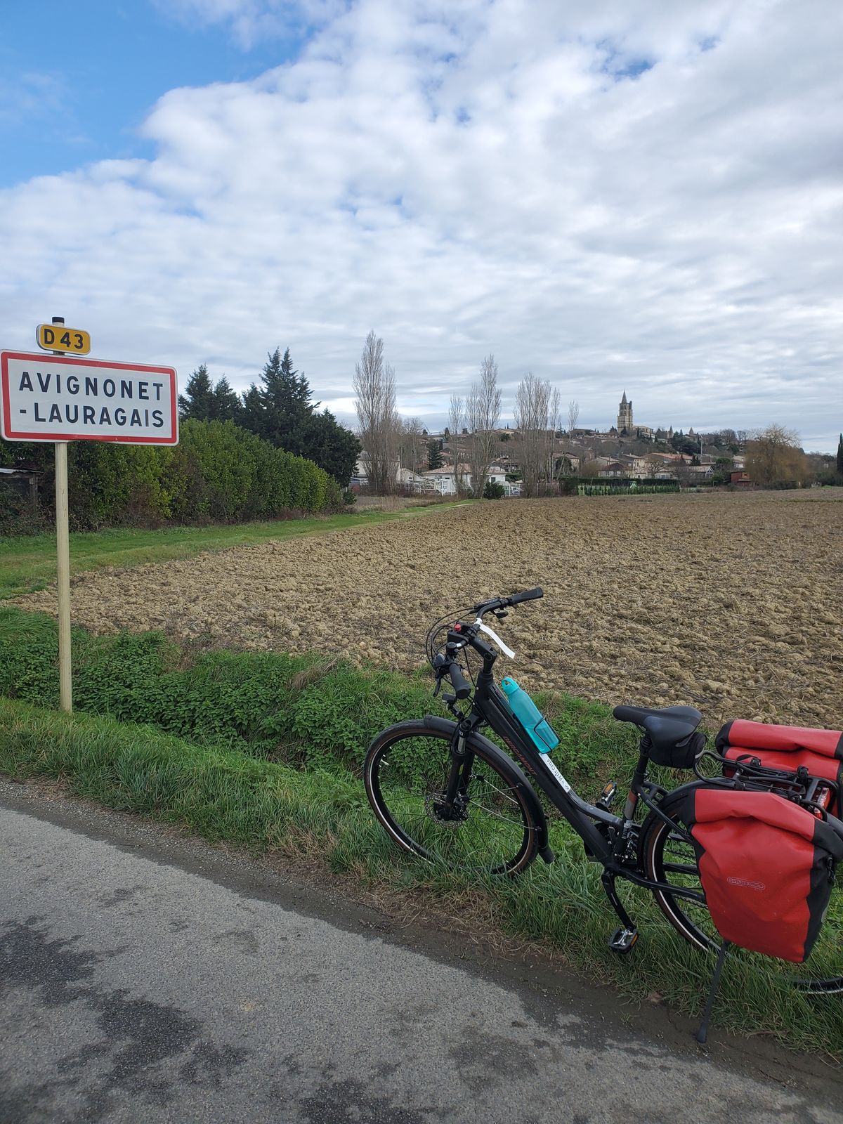 Avignonet-Lauragais town entry signpost by a road, rental bike next to it.